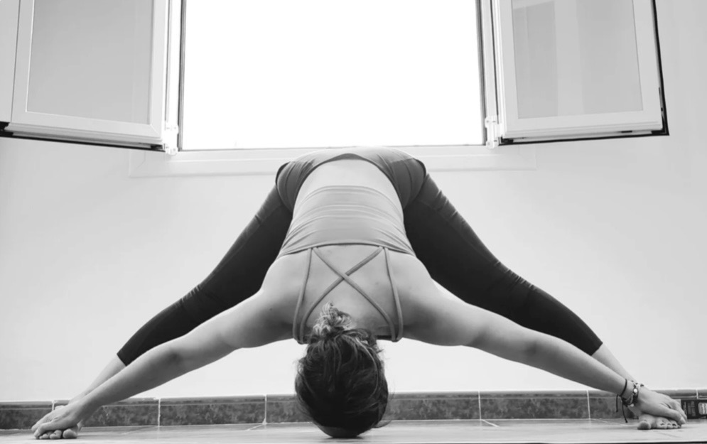 A wide legged forward fold practised in front of an open window